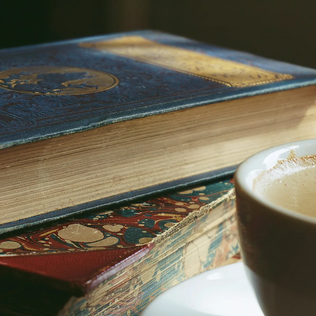 Pilha de livros vintage com xicara de cafe quente, atmosfera reflexiva e bibliografia exposta.