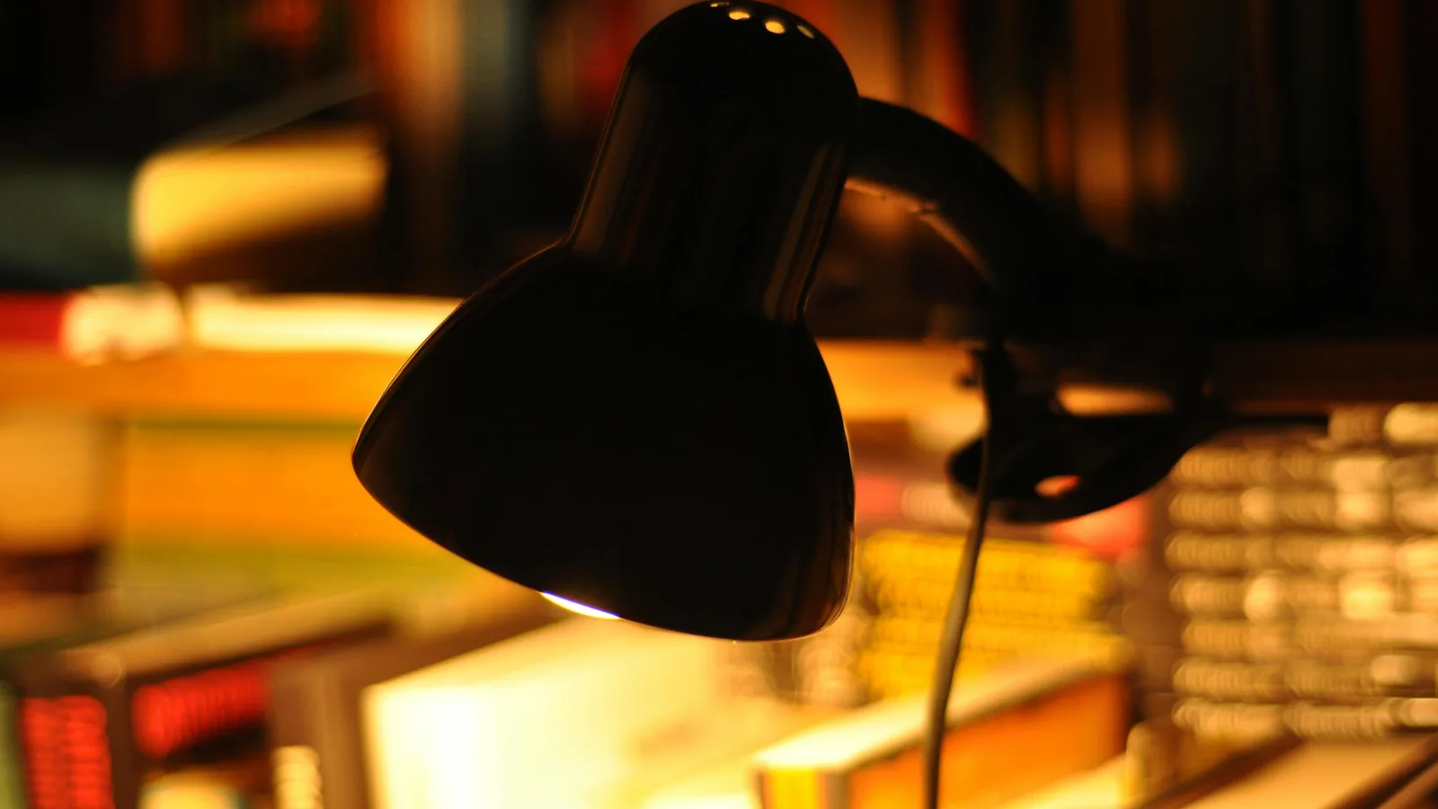 Gabinete academico com lampada de mesa iluminando pilhas de livros academicos, atmosfera de pesquisa noturna.